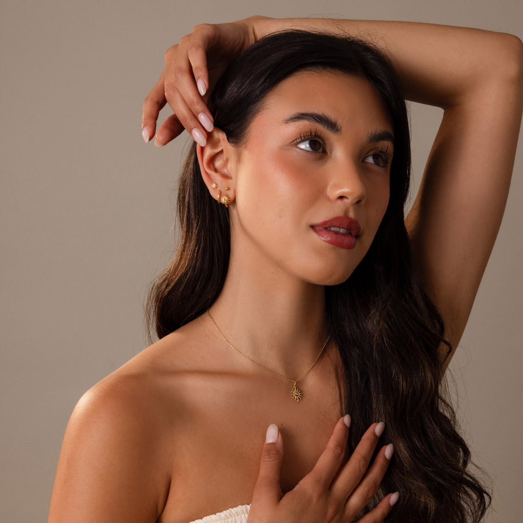 A woman with long dark hair poses in a strapless top, showcasing the radiant Celestial Sun Huggies for a bold jewelry statement.