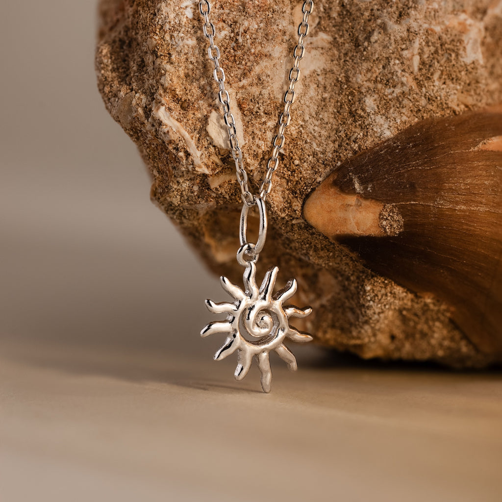 The Celestial Sun Necklace in Silver is showcased against a rough stone background, creating a striking statement piece.