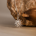 The Celestial Sun Necklace in Silver is showcased against a rough stone background, creating a striking statement piece.