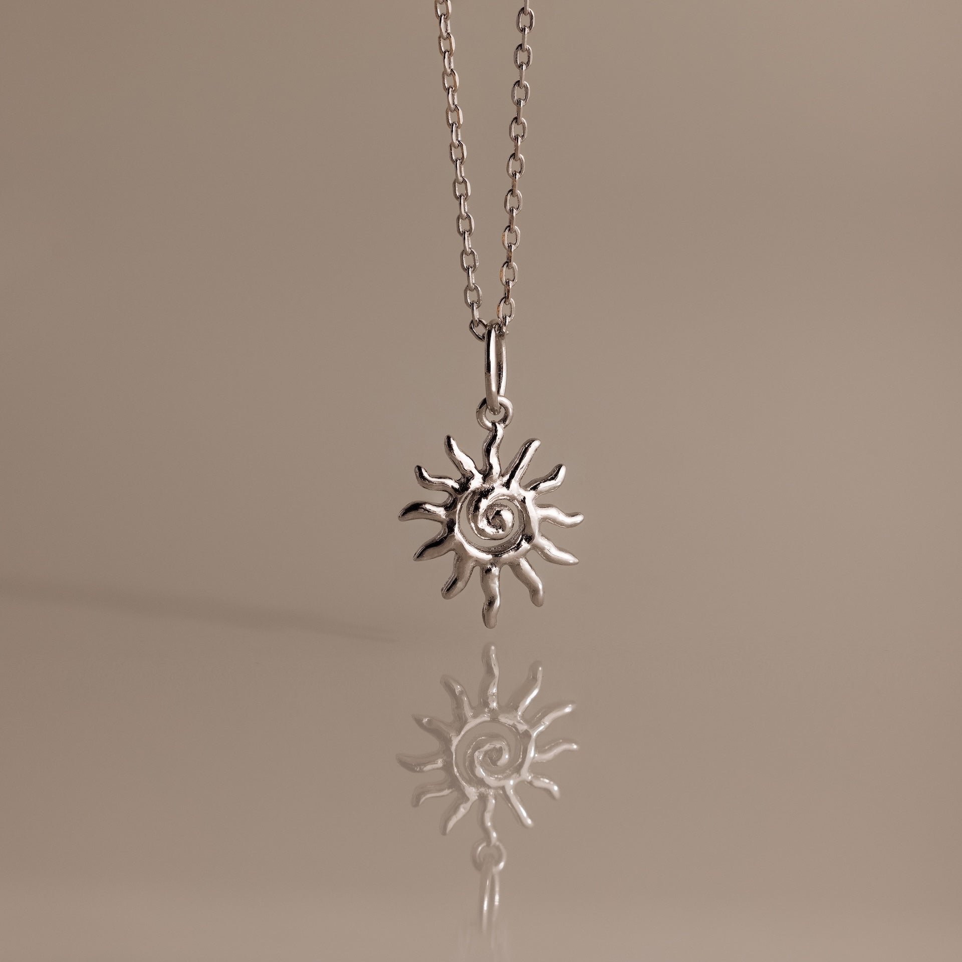 Celestial Sun Necklace in Silver with a spiral sunburst pendant, elegantly set against a soft beige background—a bold statement piece for any style.
