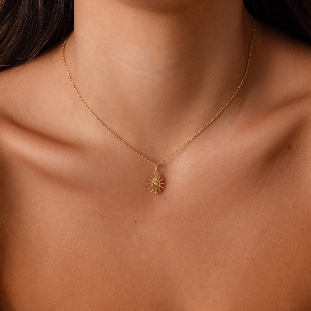 A woman wearing the Celestial Sun Necklace, a gold sunburst pendant, against bare skin and collarbones.