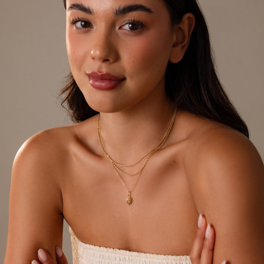 Woman with long hair poses with folded arms in a strapless white top, wearing the Celestial Sun Necklace.