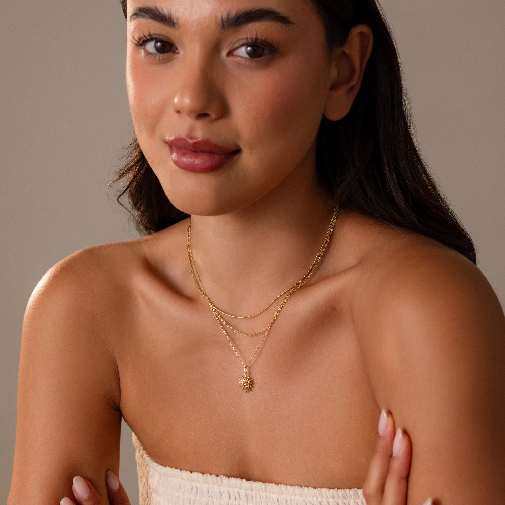Woman with long hair poses with folded arms in a strapless white top, wearing the Celestial Sun Necklace.