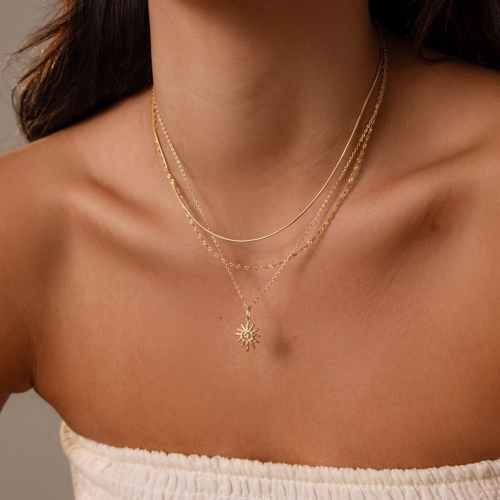 A woman wearing a white strapless top styles her look with layered gold necklaces, highlighting the Celestial Sun Necklace.