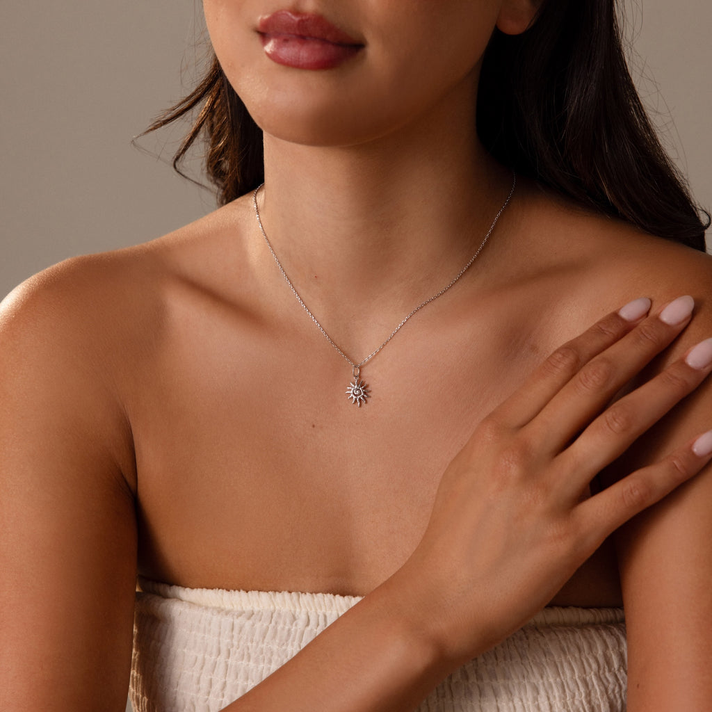 Woman wearing a strapless top and the Celestial Sun Necklace in Silver, with one hand on her collarbone.