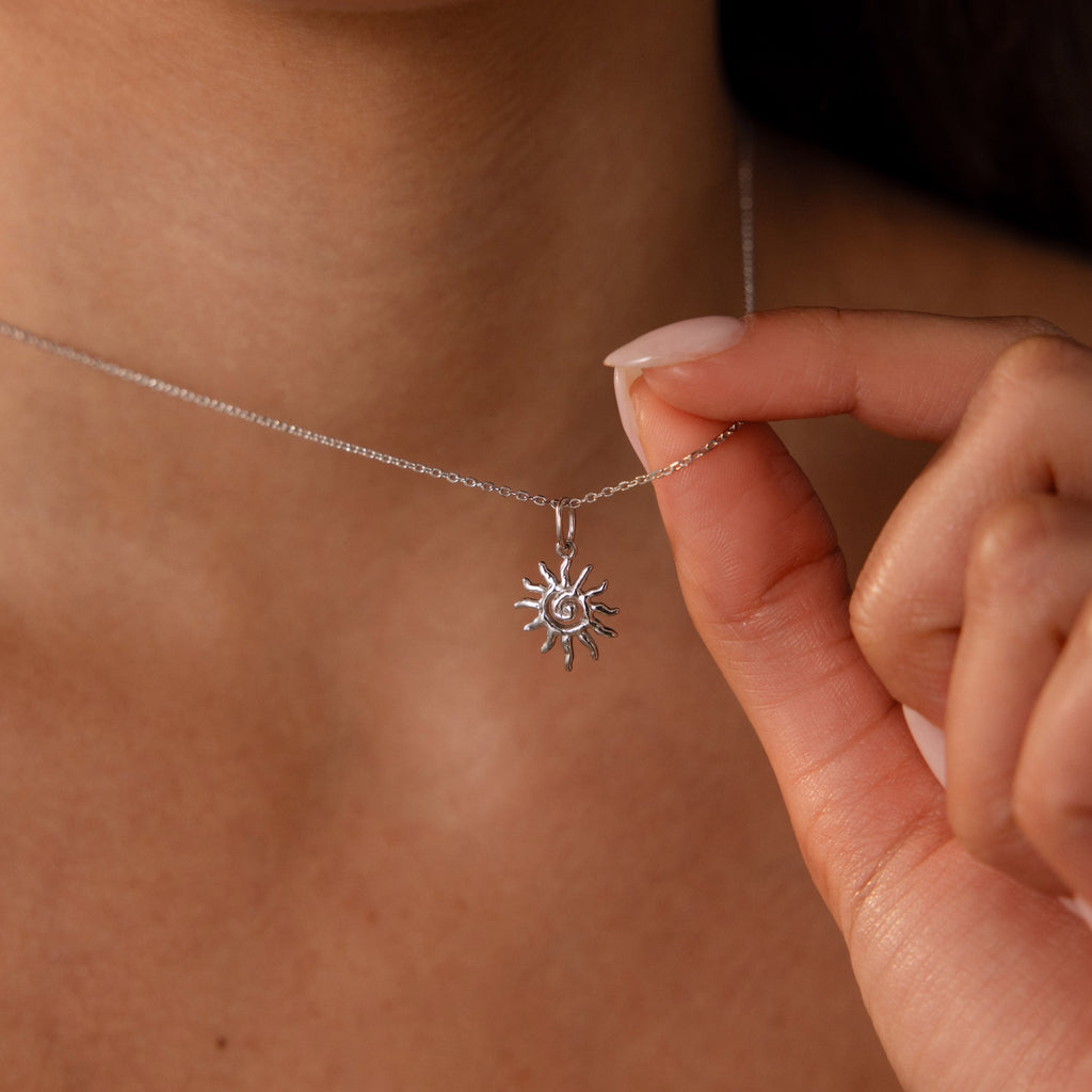 A hand holds the Celestial Sun Necklace in Silver against bare skin.