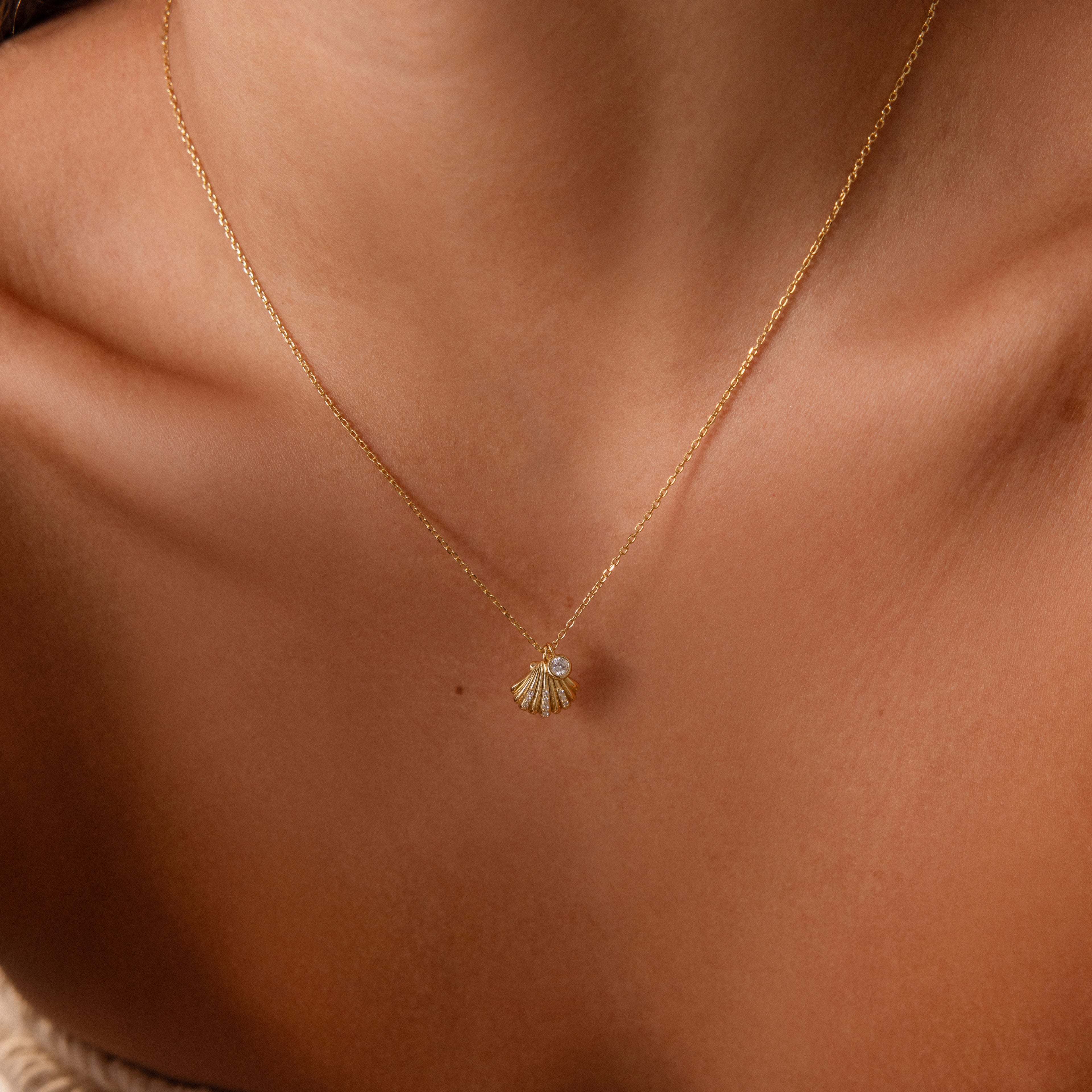 Close-up of the Diamond Seashell Charm Necklace in 18K Gold on a person’s neck, highlighting elegant coastal-inspired jewelry.