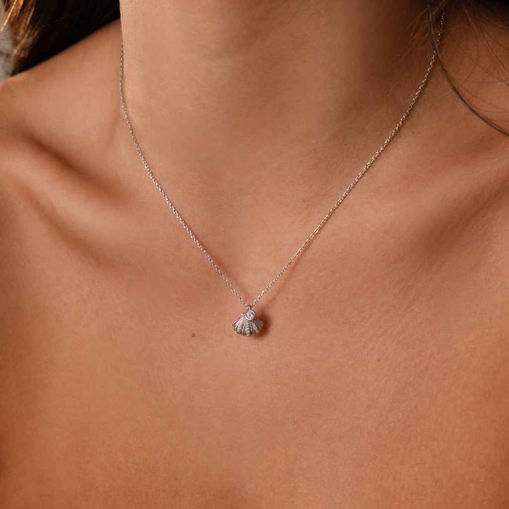 The Diamond Seashell Charm Necklace in Silver features a delicate shell pendant that adds sparkle to a womans neck and collarbone.