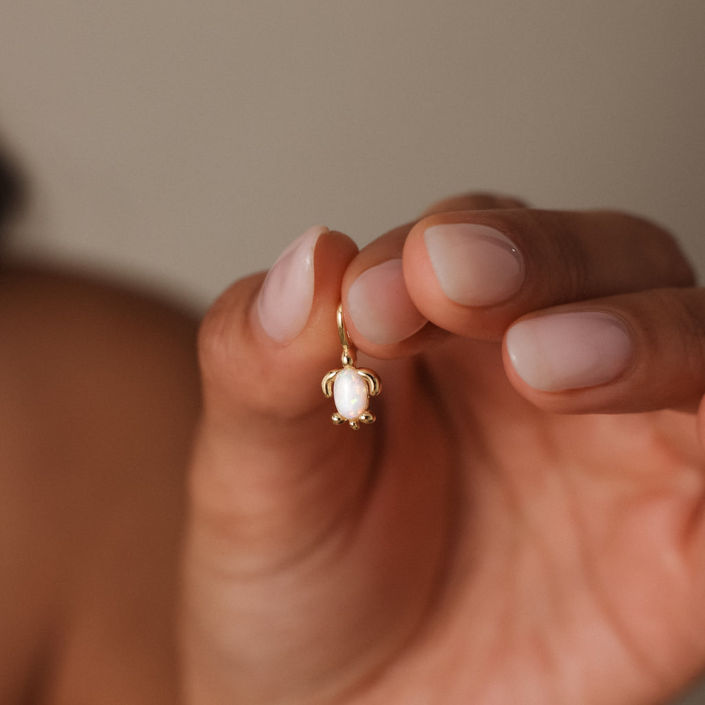 A manicured hand holds the Opal Sea Turtle Charm in 18K Gold, featuring a white oval stone that captures ocean-inspired elegance.