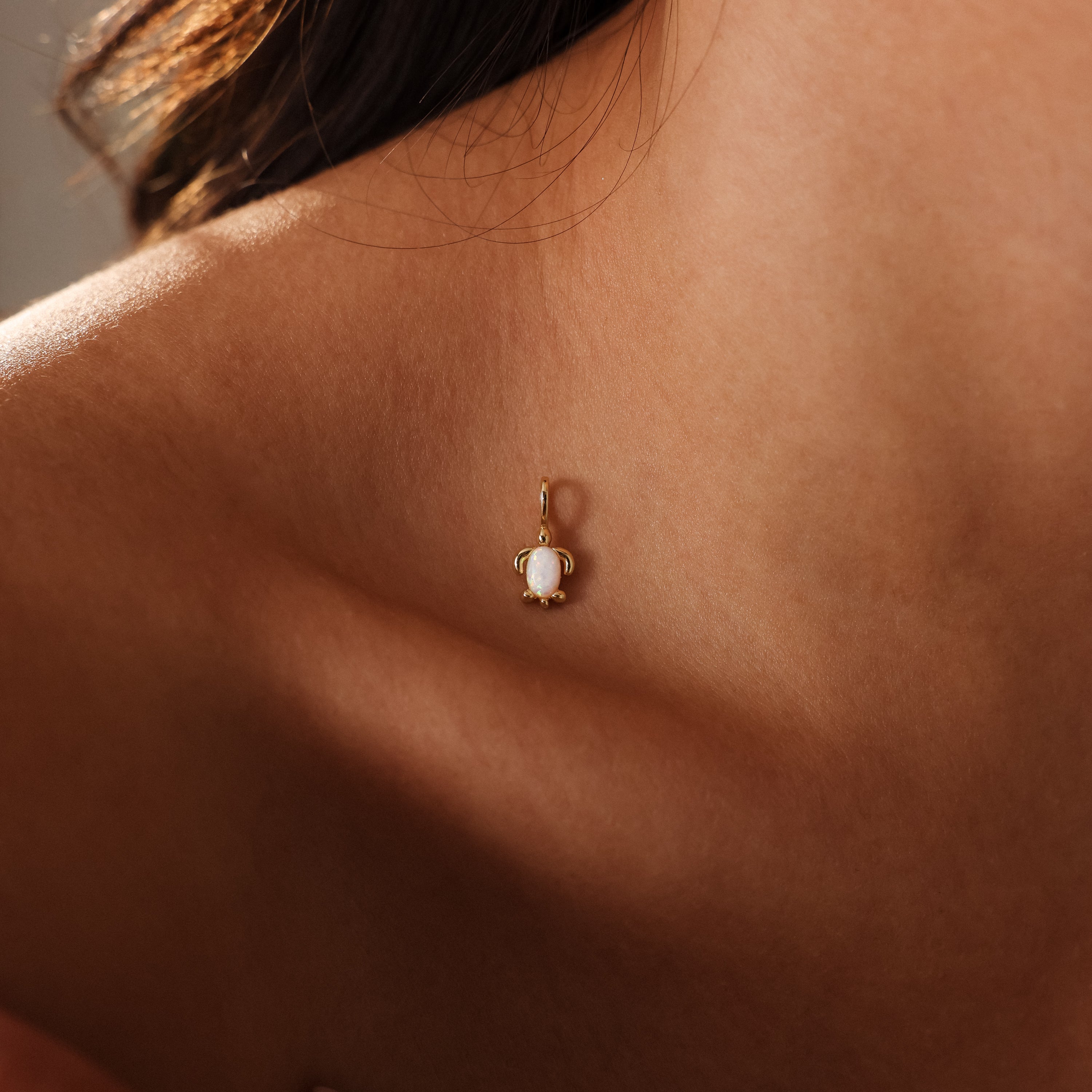 The Opal Sea Turtle Charm in 18K Gold, inspired by the seaside, rests gracefully on a person’s collarbone near their neck and shoulder.