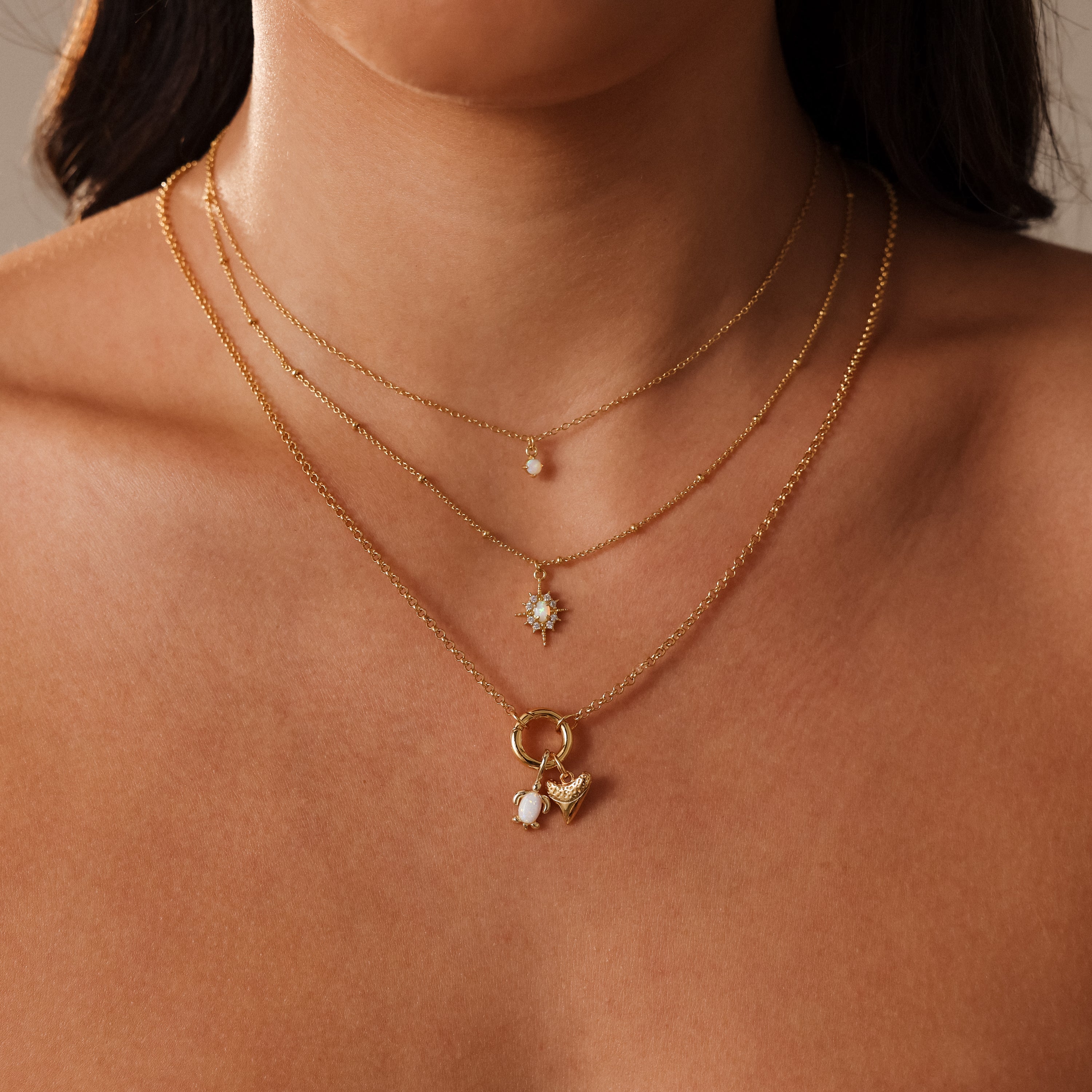 Woman wears an Opal Sea Turtle Charm in 18K Gold layered with pearl and gemstone necklaces for a delicate, ocean-inspired look against bare skin.