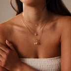 A woman in a white strapless top layers gold necklaces, including the Opal Sea Turtle Charm in 18K Gold, featuring ocean-inspired gemstone details.
