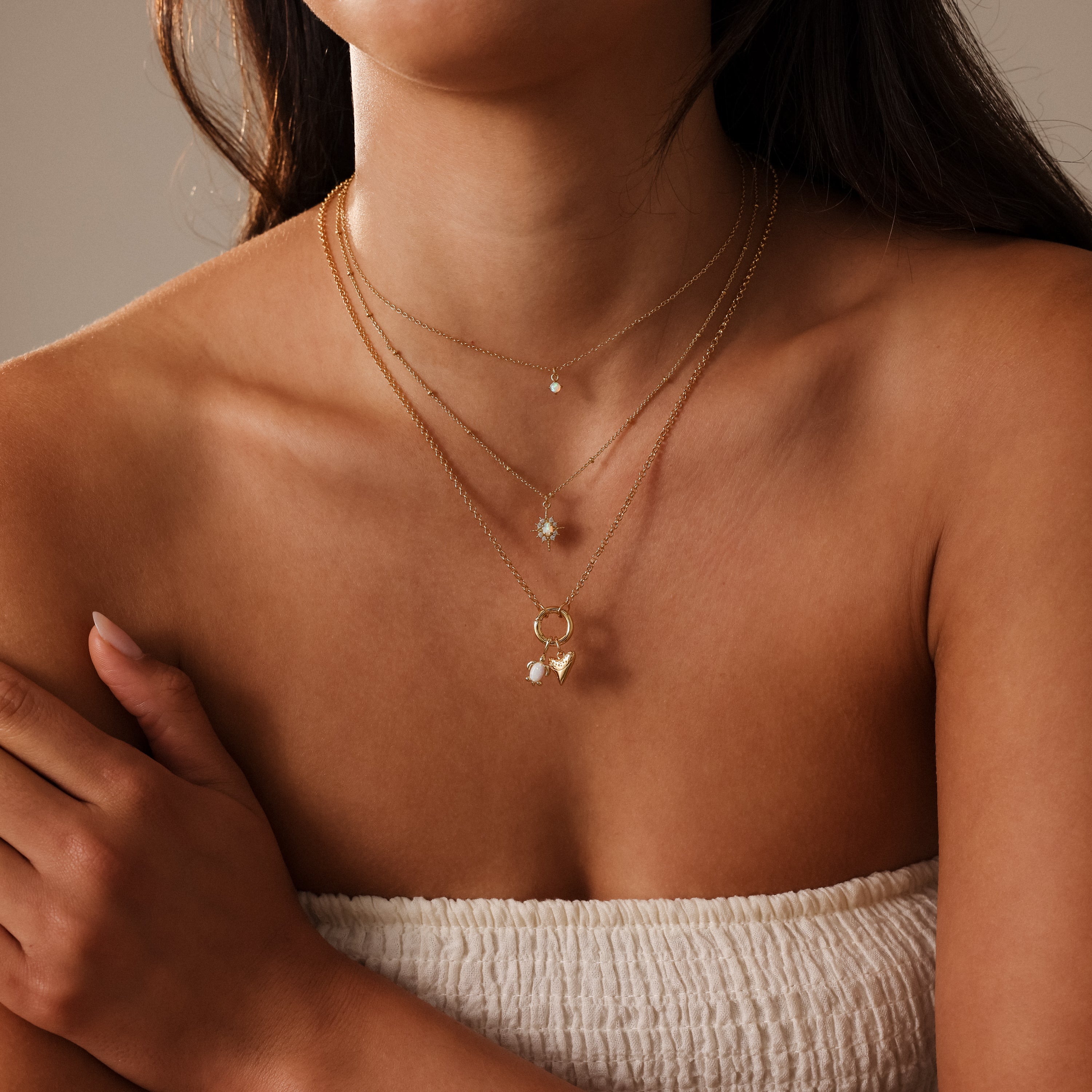 A woman in a white strapless top layers gold necklaces, including the Opal Sea Turtle Charm in 18K Gold, featuring ocean-inspired gemstone details.