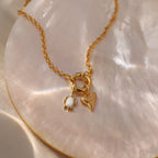 Opal Sea Turtle Charm in 18K Gold features a gold chain necklace with pearl, heart, and sea turtle charms on an iridescent shell surface for an ocean-inspired look.