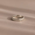 The Organic Fingerprint Band in Sterling Silver, featuring a delicate leaf pattern, rests on a soft beige surface—ideal as a memorial keepsake or custom-engraved ring for treasuring special memories.