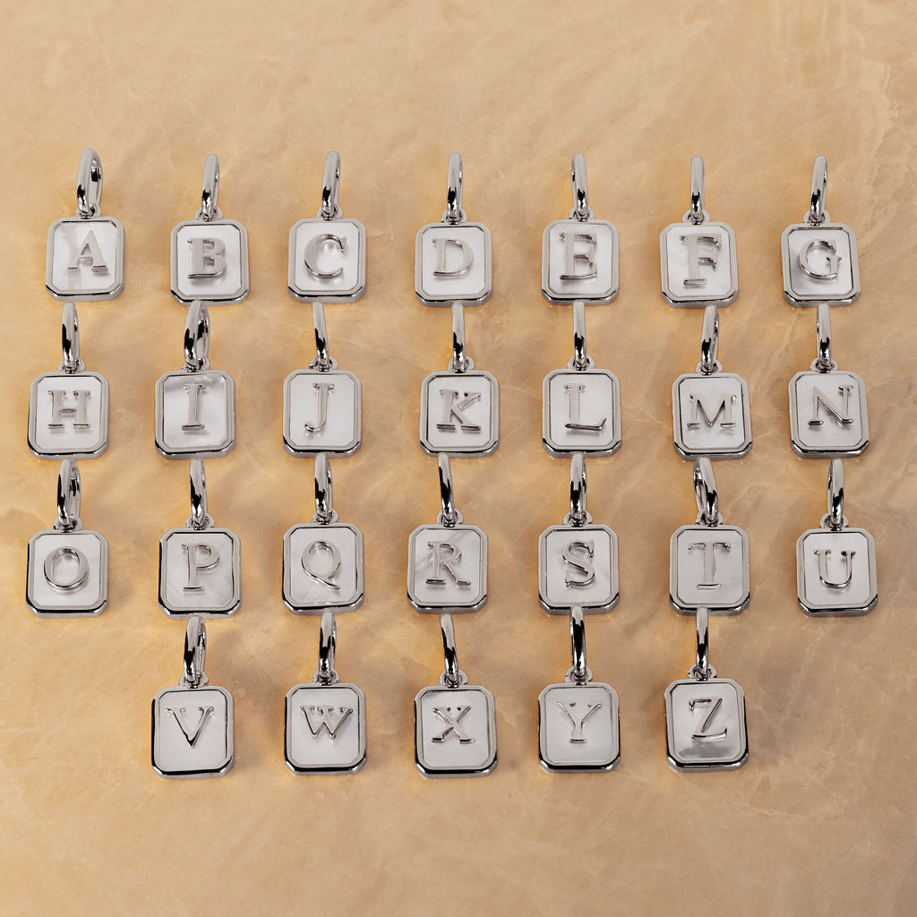 Twenty silver letter charms spelling out the alphabet, arranged in four rows of five on a textured beige background.