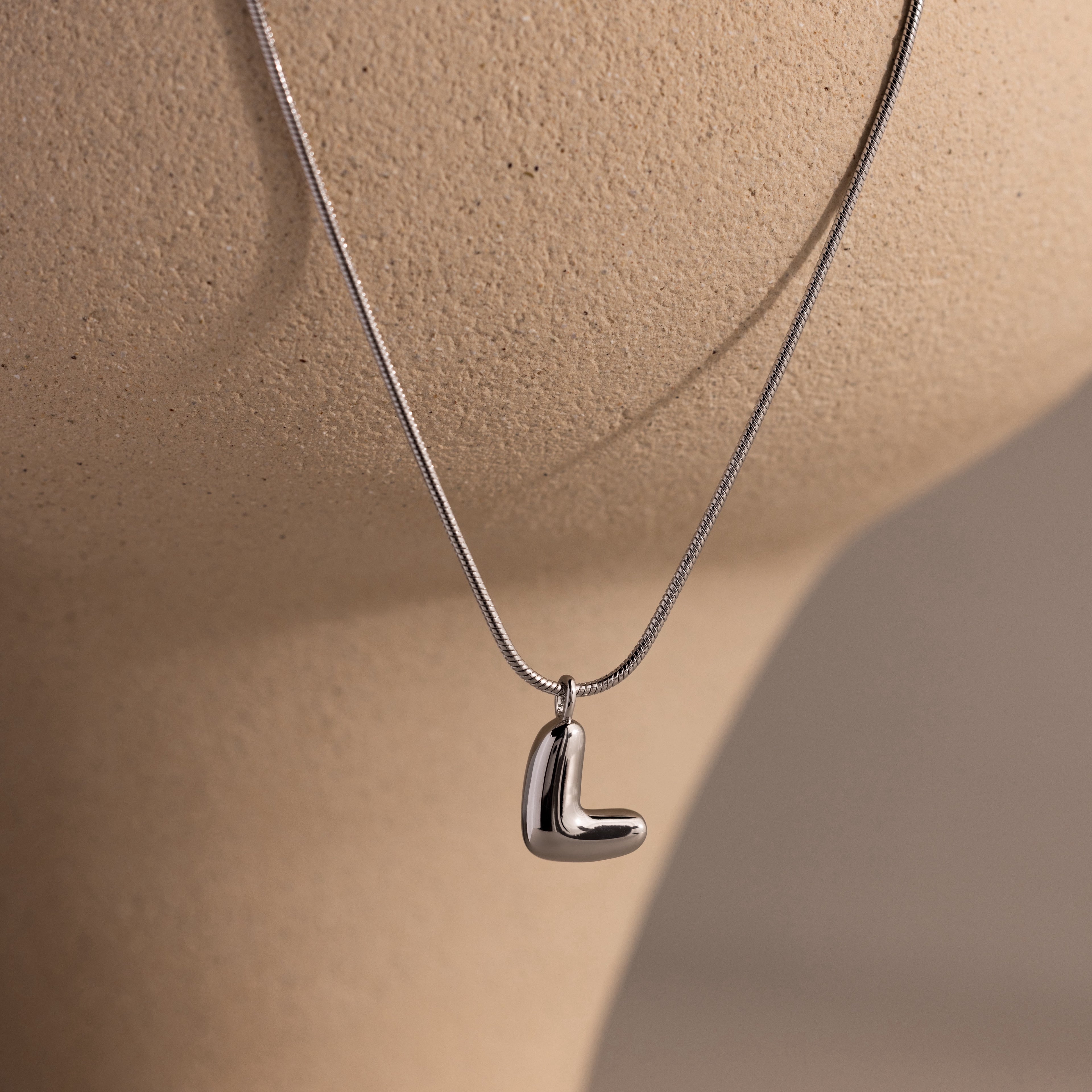 The Bubble Letter Necklace in White Gold, ideal for fans of personalized jewelry, is displayed on a beige mannequin bust.