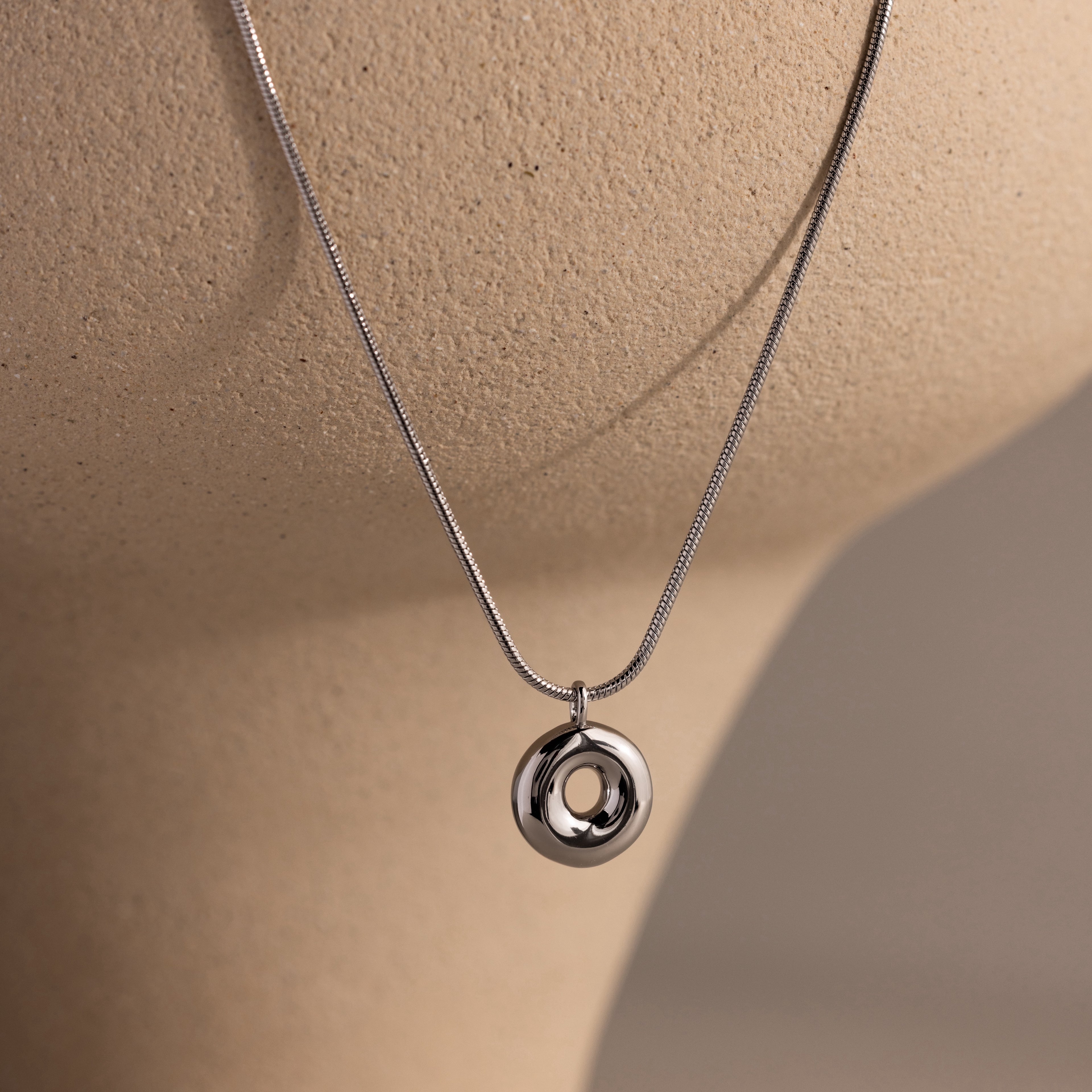 The Bubble Letter Necklace in White Gold is displayed on a beige mannequin bust against a neutral background, ideal for those who love personalized jewelry with a modern twist.