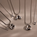 Four Bubble Letter Necklaces in White Gold, featuring chunky letter pendants A, B, and C, are displayed on a beige background—making them the perfect personalized jewelry pieces.