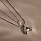 Two Bubble Letter Necklaces in White Gold with shiny letter A pendants rest on a smooth beige surface—ideal for personalized jewelry lovers or anyone seeking a classic Bubble Letter Necklace style.