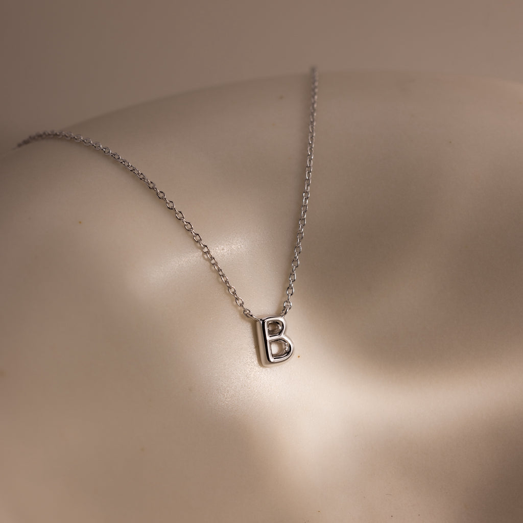 The Dainty Bubble Letter Necklace in Sterling Silver features a minimalist silver letter B pendant displayed on a smooth, light-colored surface.