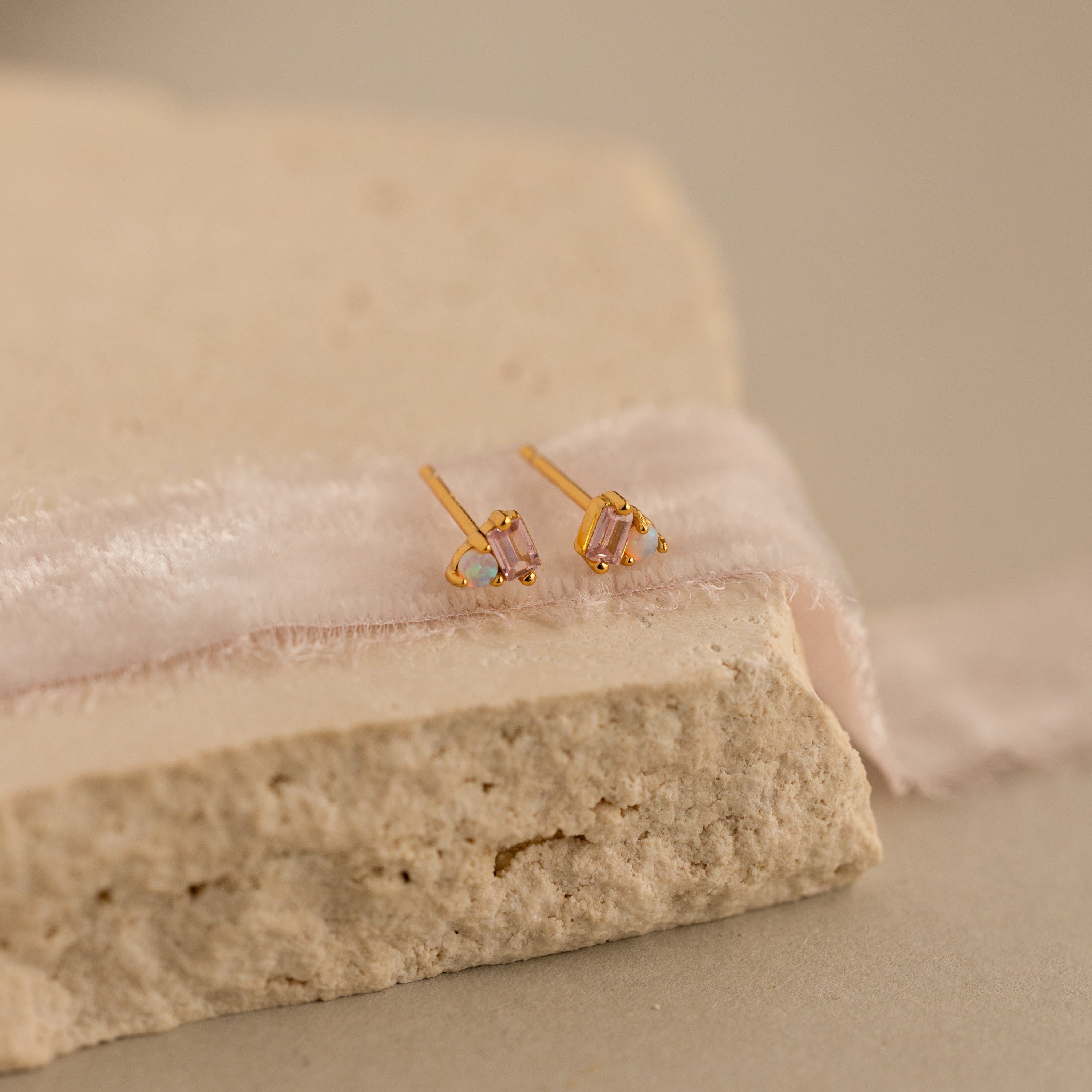 Pink Baguette Opal Studs, ideal bridal gifts, showcased on a textured stone surface with a soft pink fabric ribbon.