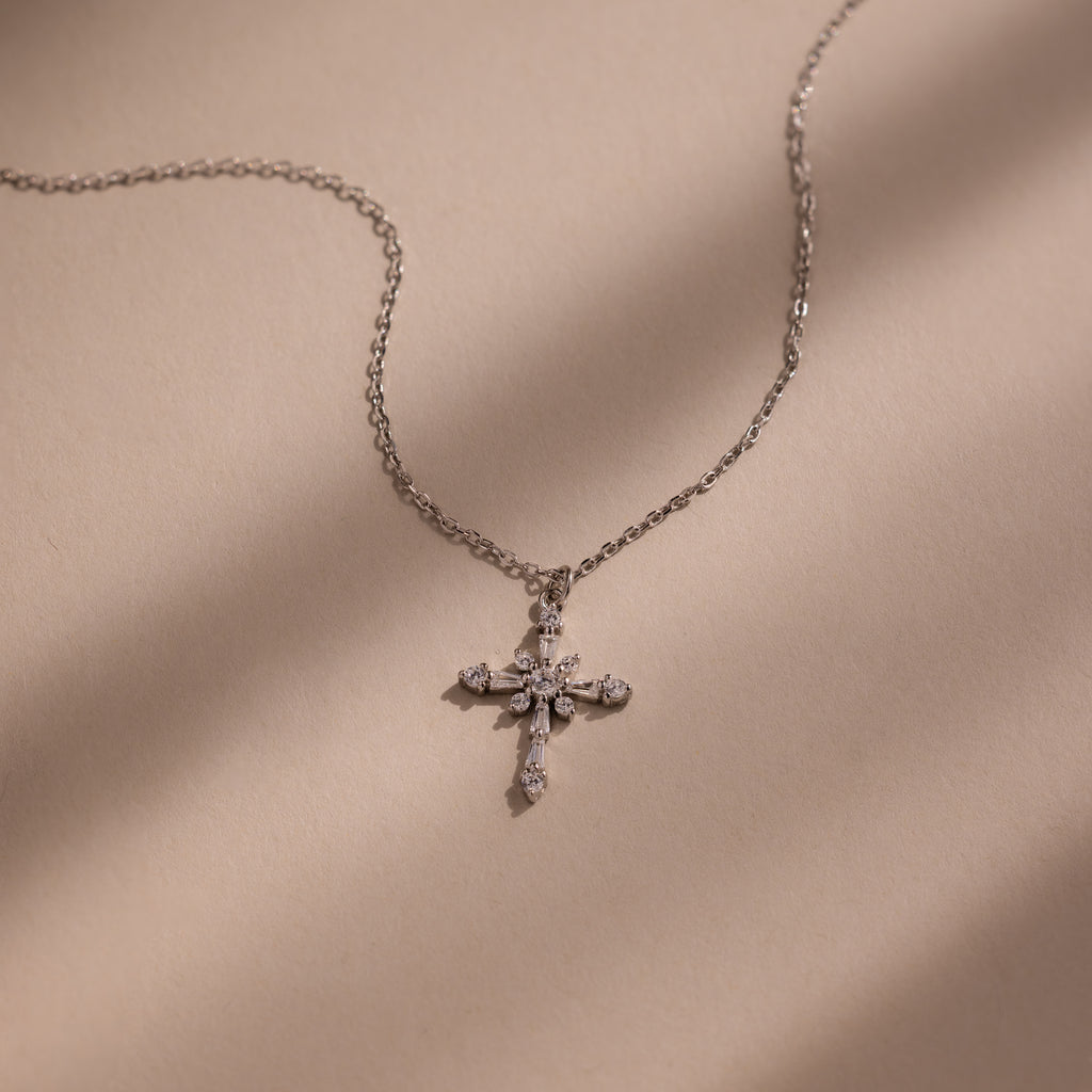 The Vintage Diamond Cross Necklace in Silver is displayed on a beige surface with soft shadow lines.
