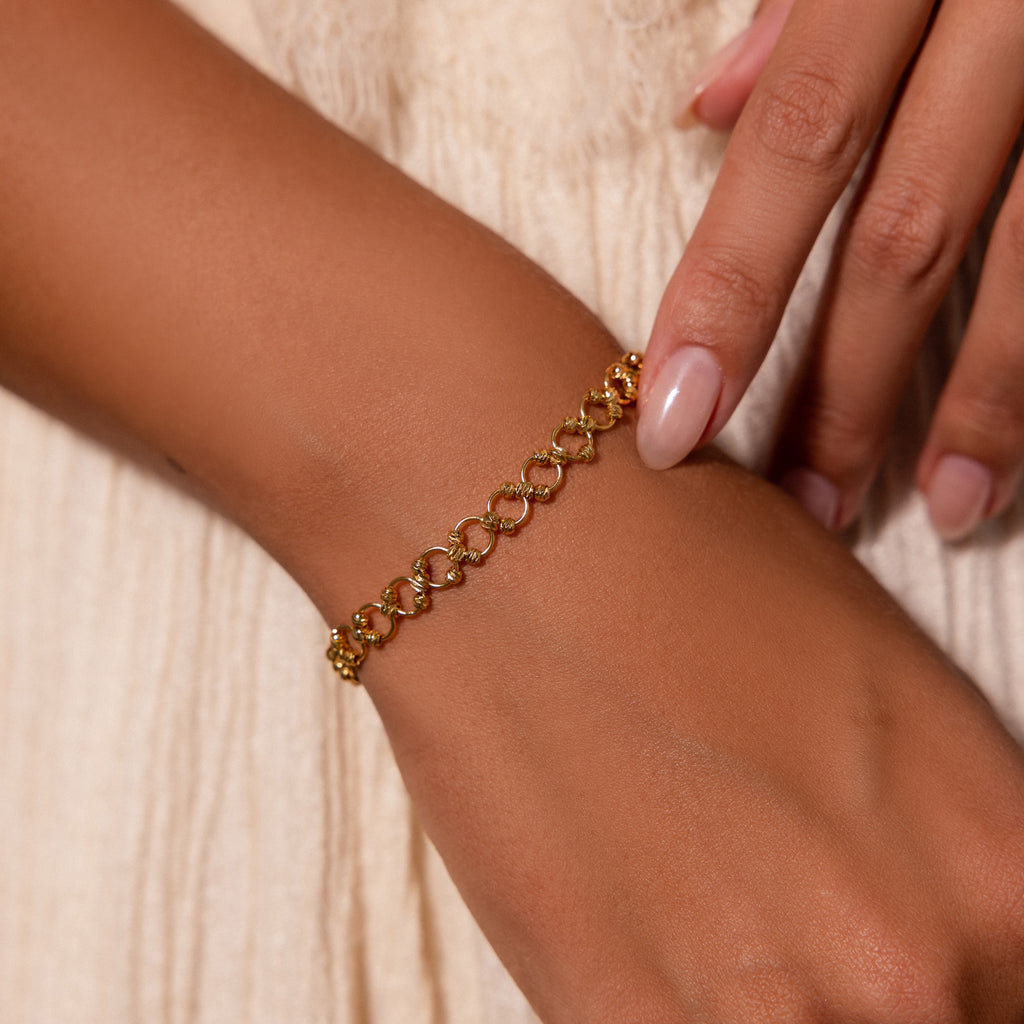 A manicured hand wears the Orbit Chain Bracelet in 18K Gold against a cream fabric, showcasing the elegance of this stunning jewelry piece.