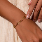 A manicured hand wears the Orbit Chain Bracelet in 18K Gold against a cream fabric, showcasing the elegance of this stunning jewelry piece.