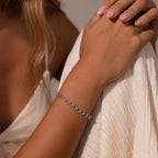 A womans hand showcases the Orbit Chain Bracelet in Silver, resting on white textured fabric and paired with a white dress for a refined touch of elegance.