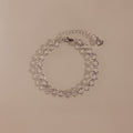 The Orbit Chain Bracelet in Silver features delicate heart-shaped links and an adjustable chain, showcased on a beige background—ideal for fans of elegant jewelry.