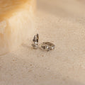 Pearl Diamond Cluster Huggies in Sterling Silver, reminiscent of elegant pearl and diamond earrings, displayed on a light, textured stone surface.