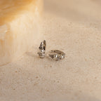 Pearl Diamond Cluster Huggies in Sterling Silver, reminiscent of elegant pearl and diamond earrings, displayed on a light, textured stone surface.