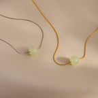 Close-up of a two dainty chain necklaces in gold and silver, each featuring a single round green jade bead, displayed against a neutral surface.