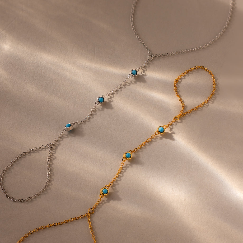 Two Turquoise Hand Chain Bracelets, one in silver and one in gold, each accented with turquoise stones, are displayed on a beige surface—the perfect set for fans of the Turquoise Hand Chain Bracelet.