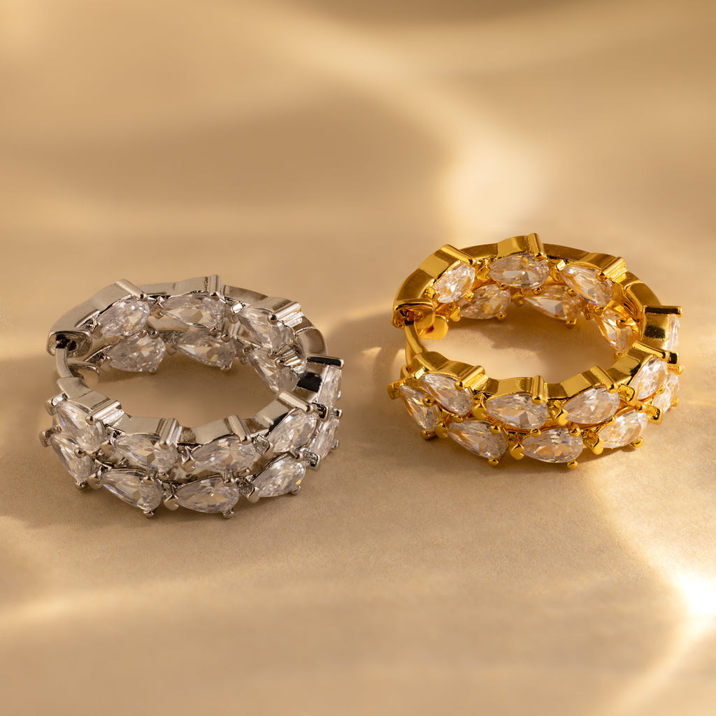 The Inside Out Pear Diamond Hoops in Silver, adorned with sparkling pear-cut stones, make a perfect bridesmaid gift and rest elegantly on a soft beige surface.