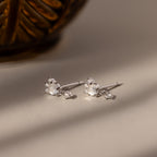 The Halo Moonstone Drop Studs in Sterling Silver showcase luminous moonstones and sparkling accents, radiating royal elegance on a light surface.
