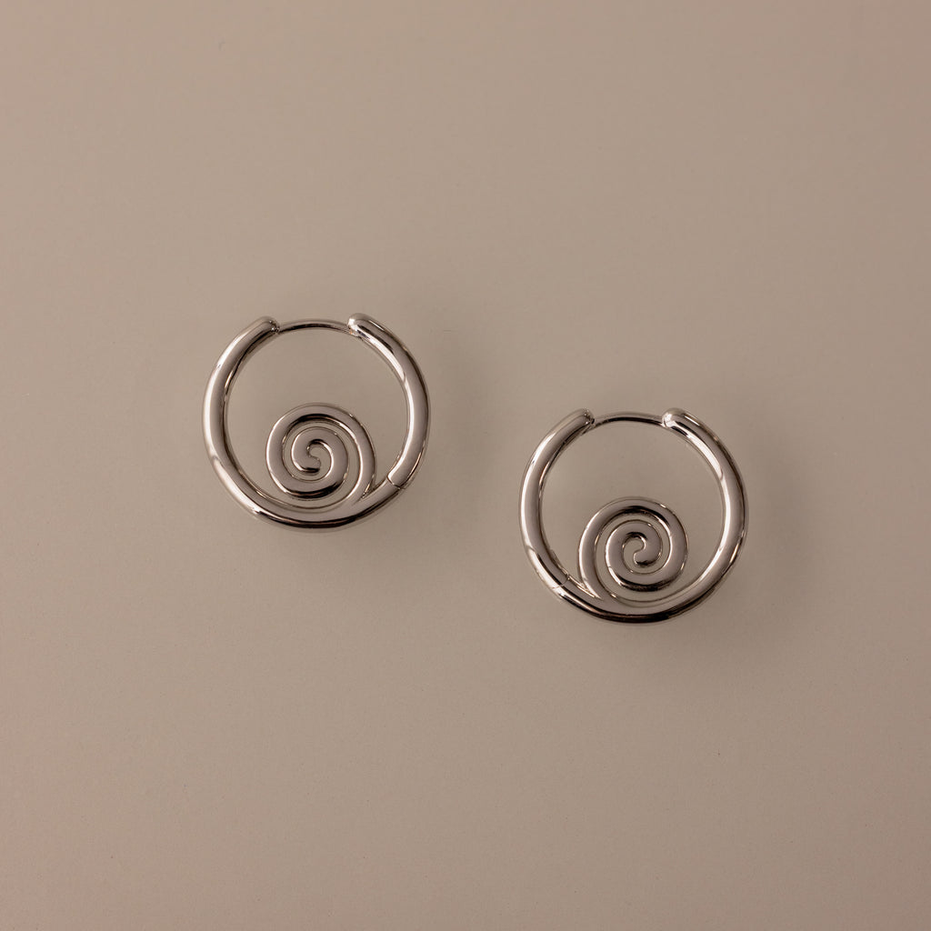 Spiral Swirl Hoops in Silver with intricate spiral designs rest on a light beige background—perfect boho earrings for your next beach vacation jewelry collection.