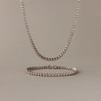 The Diamond Bezel Tennis Necklace & Bracelet Set in White Gold, displayed on a beige background, makes an elegant and unforgettable anniversary gift.