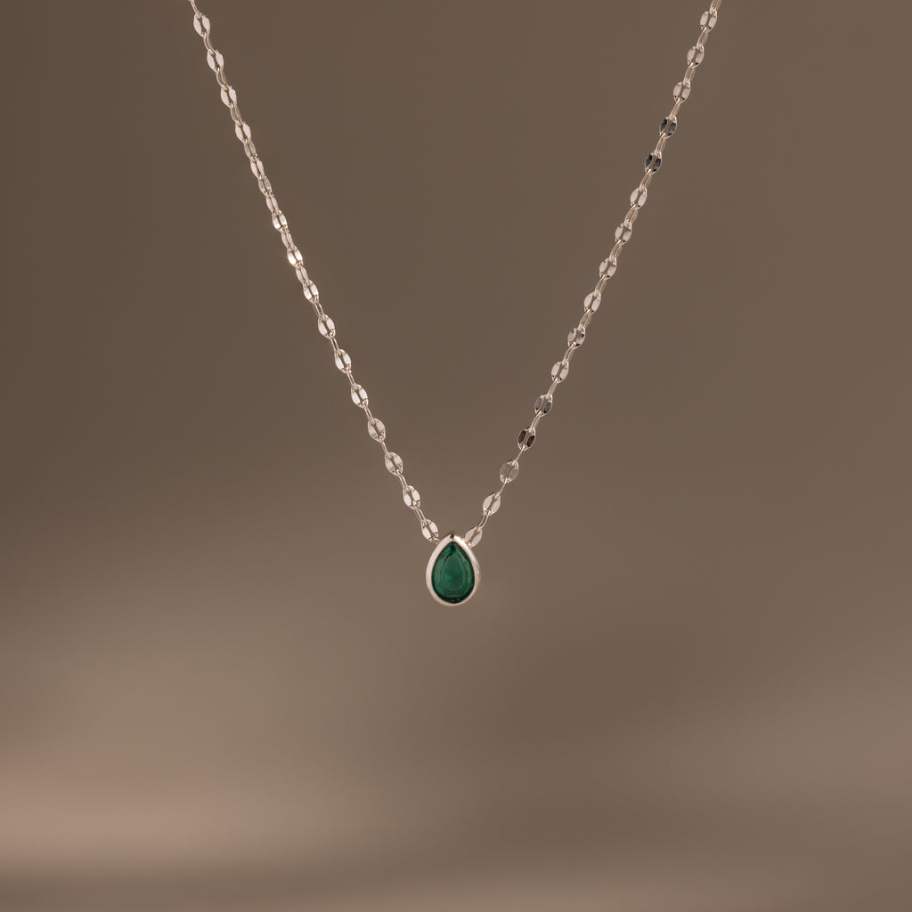 The Multiple Teardrop Birthstone Necklace in Sterling Silver features a delicate chain with small green pendants, displayed on a plain beige background—an elegant keepsake jewellery piece ideal for everyday wear.