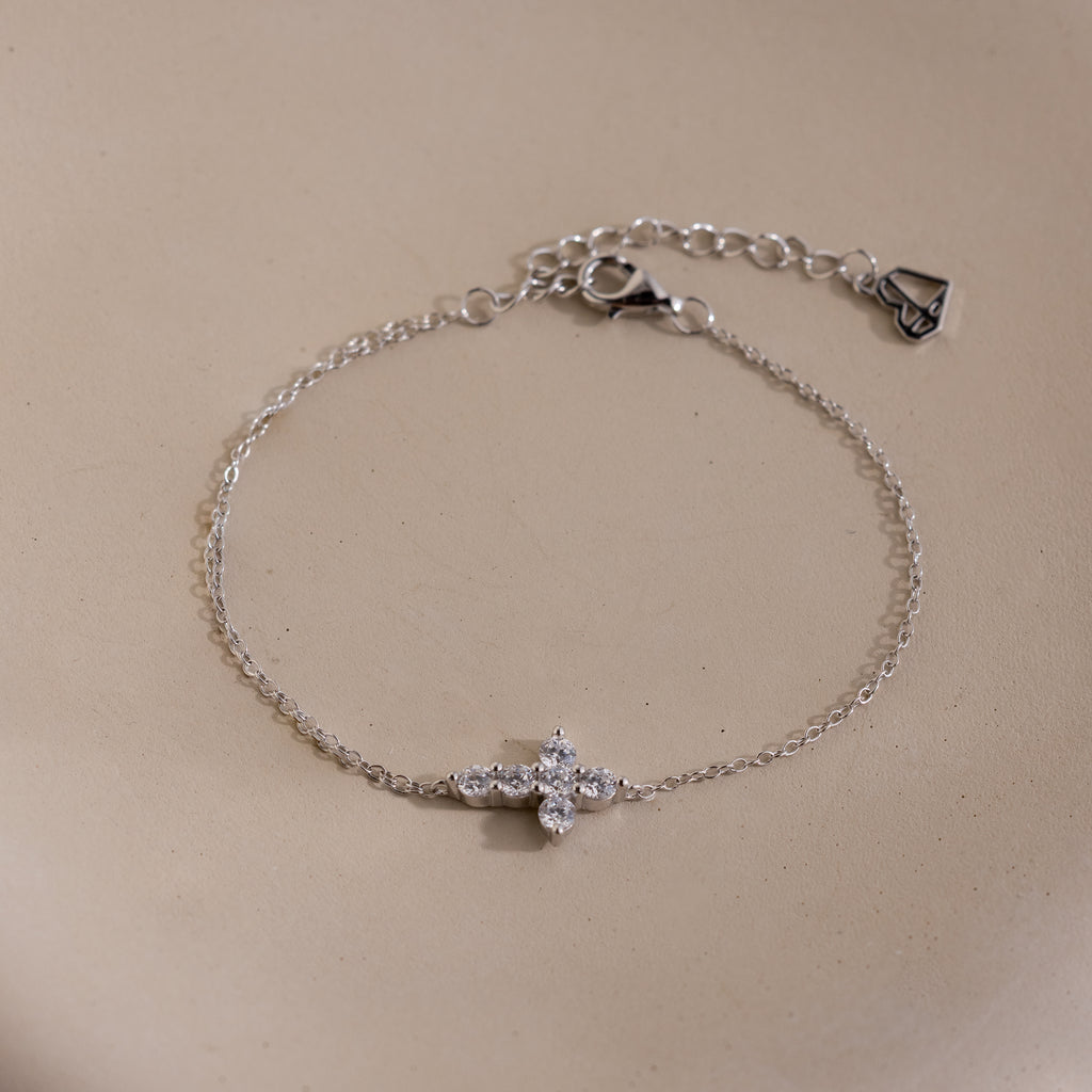 Silver chain bracelet with an adjustable clasp, featuring a cross shaped charm set with small round white gemstones.