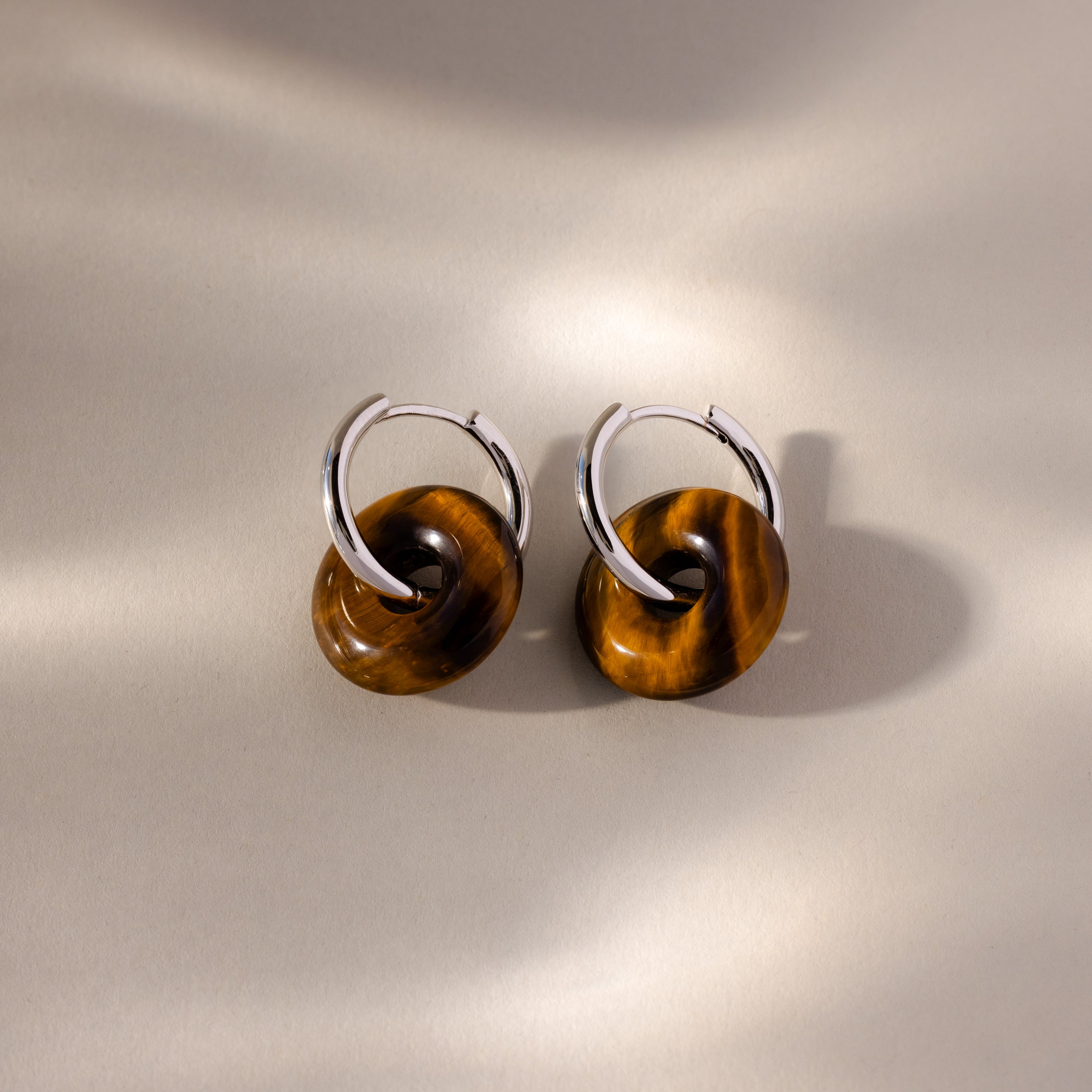 Tiger's Eye Duo Hoops: Silver hoop earrings feature brown circular accents, reminiscent of Tiger’s Eye, displayed on a neutral, softly lit background.