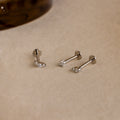 The Tiny Diamond Flatback Studs Set in Sterling Silver features three dainty earrings with clear gemstones, displayed on a light beige surface.
