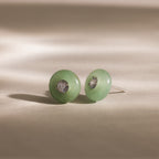 Close-up of round green jade stud earrings featuring a sparkling CZ diamond center and silver bezel setting, displayed on a neutral background.