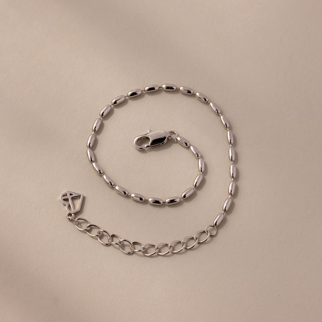 The Oval Beaded Bracelet features silver oval links and polished beads with a lobster clasp, displayed on a beige surface—ideal for fans of modern classic jewelry.