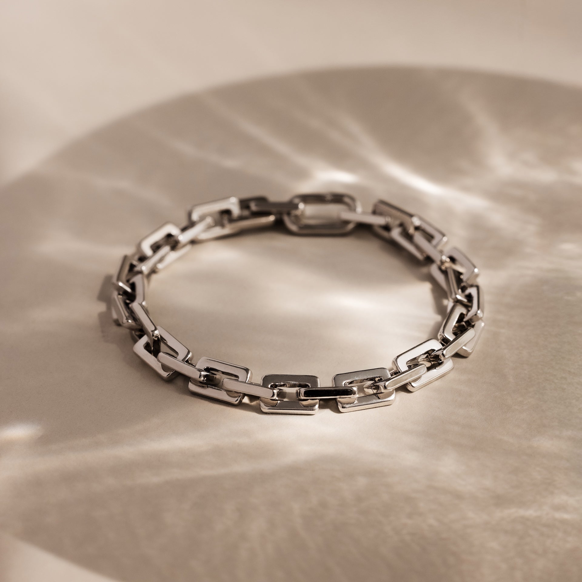 The Eternal Link Bracelet in Silver showcases a modern geometric design, elegantly displayed on a light surface with soft, reflective shadows.