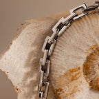 The Eternal Link Bracelet in Silver, a true modern essential, draped over a textured, fossil-like stone background.
