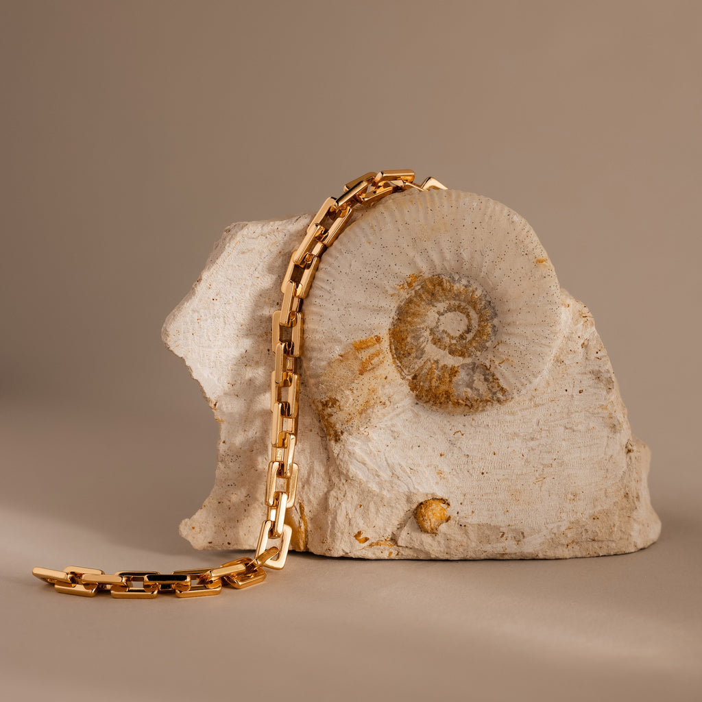 The Eternal Link Bracelet in 18K Gold draped over a beige fossilized rock with a spiral shell pattern—modern essentials meet timeless beauty.