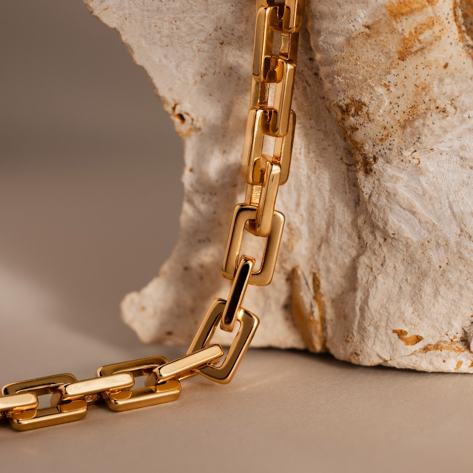 The Eternal Link Bracelet in 18K Gold drapes over textured stone, showcasing its modern geometric design and timeless elegance.