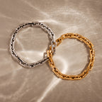 The Eternal Link Bracelet, in both silver and gold, arranged on a softly textured beige surface with light reflections—perfect modern essentials.